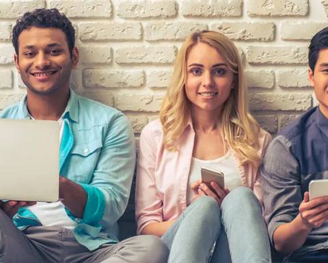 Un grupo de jóvenes sonrientes sentado juntos, usando dispositivos electrónicos.