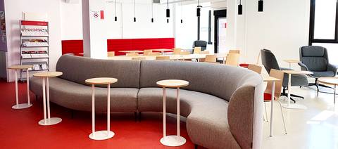 Una sala de estudio moderna y luminosa con muebles confortables y mesas pequeñas.