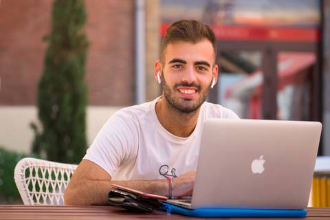 Un joven sonriente trabaja en su computadora portátil en un ambiente exterior.