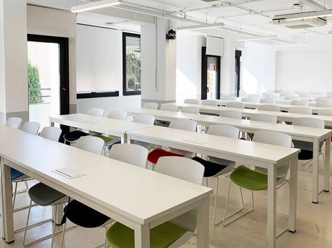 El aula está equipada con mesas y sillas en un ambiente iluminado y moderno.