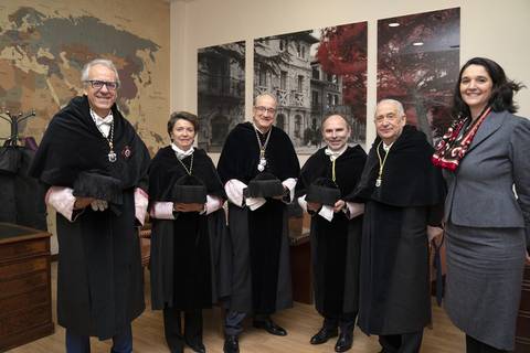 Un grupo de seis personas vestidas con togas y medallas posan en un interior con decoración elegante.
