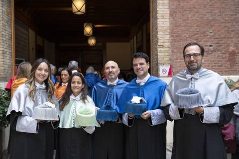 Un grupo de cinco personas vestidas con túnicas y gorros ceremoniales posan juntos en un evento académico.