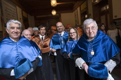 Un grupo de personas con capas azules y accesorios ceremoniales posan juntos en un ambiente institucional.