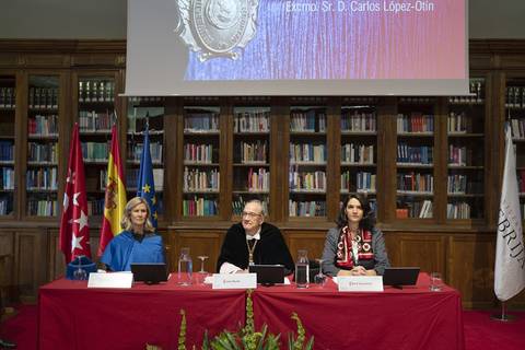 Una mesa redonda con tres ponentes frente a un fondo de estanterías llenas de libros y banderas.