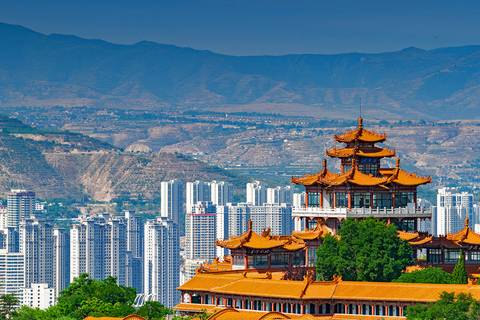 Una vista panorámica de un edificio tradicional con techos en punta frente a un paisaje urbano moderno y montañoso.