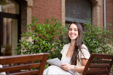 Una mujer sonriente sentada en un banco al aire libre con papeles en las manos.