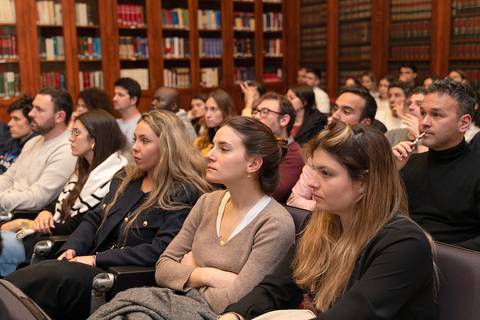 Un grupo de personas asistiendo a una conferencia en una sala con estanterías de libros.