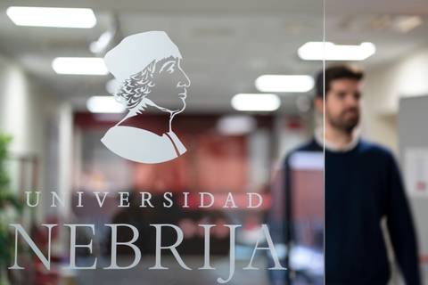 En la imagen se observa el logotipo de la Universidad Nebrija en una puerta de vidrio, con un hombre de fondo.