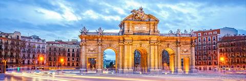 La imagen muestra una vista del Arco de la Entrada, una emblemática estructura arquitectónica en una ciudad con luces y un cielo nublado.
