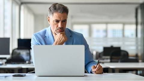Un hombre de negocios parece concentrado mientras trabaja en su computadora portátil en una oficina moderna.