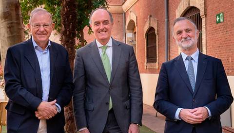 Tres hombres de pie en un entorno al aire libre, sonriendo y vistiendo trajes formales.