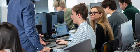 Un grupo de estudiantes trabaja en sus computadoras mientras un instructor les habla.