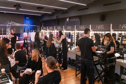 Una sala de maquillaje con varias personas preparándose y trabajando en un evento.