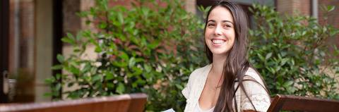 Una mujer sonriente sentada en un entorno al aire libre rodeada de vegetación.