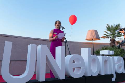 Una mujer de pie en un escenario con un globo rojo y un gran cartel que dice 'UNebrija'.