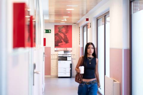 Una mujer camina por un pasillo con impresoras y una obra de arte roja en la pared.