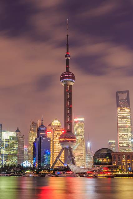 La imagen muestra la Torre de Shanghai iluminada durante la noche, rodeada de edificios modernos en una ciudad vibrante.