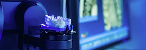 Imagen de un modelo dental sobre un soporte con luz azul y una pantalla de fondo.