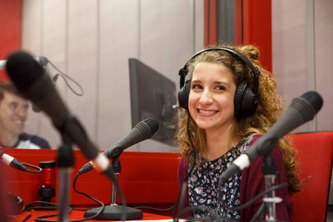 Una joven sonriente con auriculares se encuentra en un estudio de grabación.