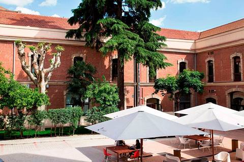 Un patio con árboles y sombrillas, rodeado de una arquitectura de ladrillo rojo.