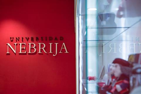 La imagen muestra el letrero de la Universidad Nebrija en un fondo rojo.