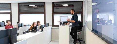 Un profesor imparte una clase a un grupo de estudiantes en un aula moderna.