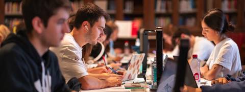 Un grupo de estudiantes concentrados trabajando en sus computadoras en una biblioteca.