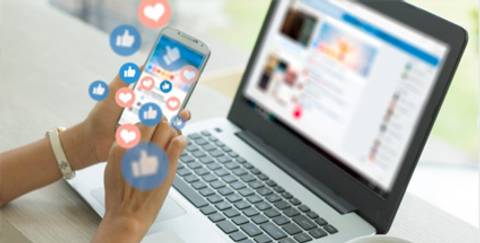 Una persona usa un teléfono móvil mientras interactúa con redes sociales en una computadora portátil.