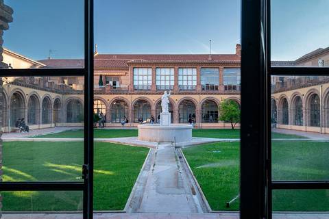 Vista de un patio histórico con una fuente central y estátuas, rodeado de arcos y construcciones antiguas.
