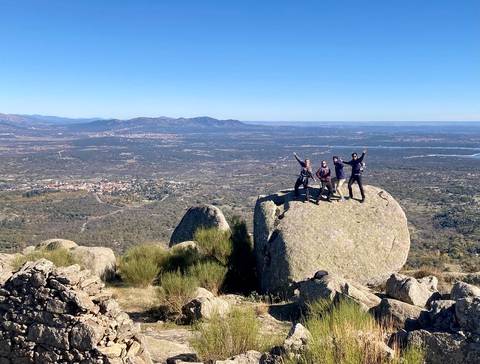 Un grupo de personas posando en una gran roca con un paisaje de montañas y valles de fondo.