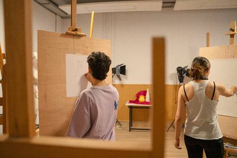 Dos personas dibujando en caballetes en un ambiente artístico.