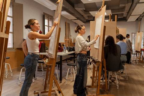 Un grupo de estudiantes está trabajando en un aula de arte, dibujando en caballetes.