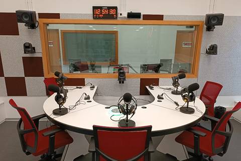 Una sala de grabación de radio con micrófonos y sillas alrededor de una mesa circular.