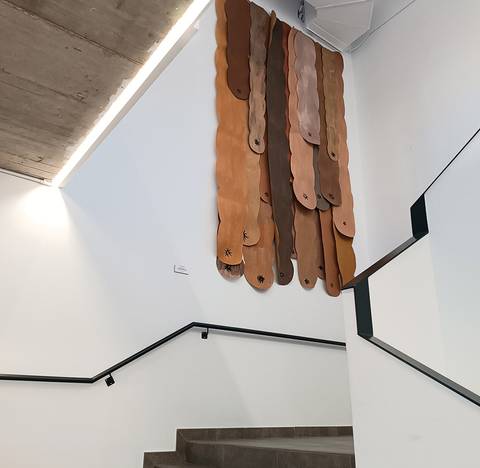 Instalación artística con formas orgánicas en tonos marrones colgando de una pared en una escalera.