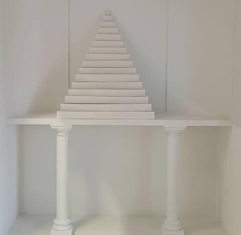 Una estructura blanca en forma de pirámide se eleva sobre una mesa sostenida por dos columnas.