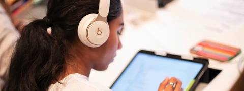 Una persona joven utiliza unos auriculares mientras interactúa con una tableta.