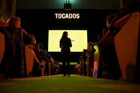Una persona de pie frente a una pantalla en un evento con el título 'TOCADOS'.