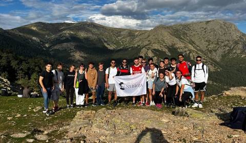 Grupo de jóvenes posando en la montaña con una bandera de la Universidad Nebrija.