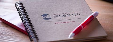 Un cuaderno de la Universidad Nebrija con un bolígrafo rojo sobre una mesa de madera.