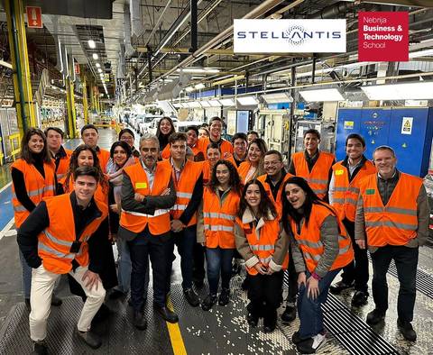 Grupo de personas sonriendo en un entorno industrial, vistiendo chalecos de seguridad naranjas.