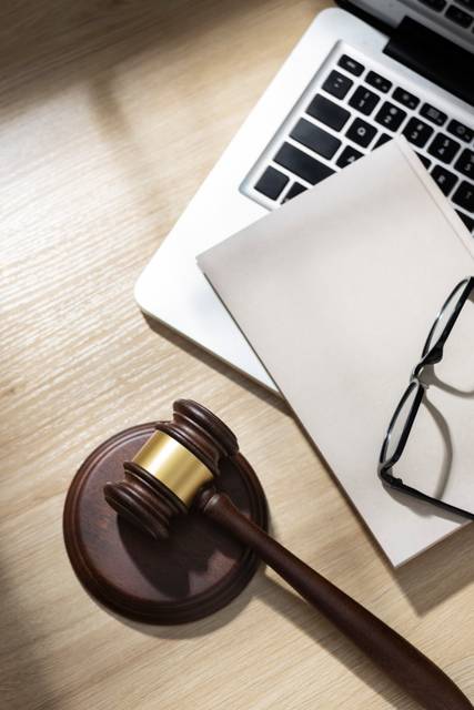 Una mesa con un martillo de juez, unas gafas y una hoja en blanco junto a un ordenador portátil.