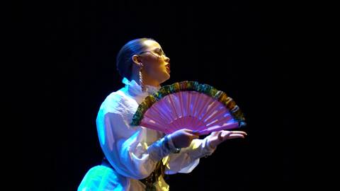 Una mujer elegante sostiene un abanico mientras posa con gracia en el escenario.