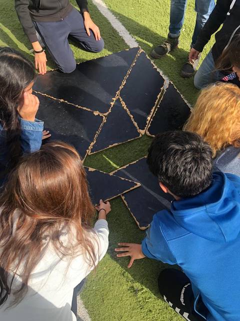 Un grupo de jóvenes está trabajando juntos para ensamblar una figura hecha de piezas sobre el césped.