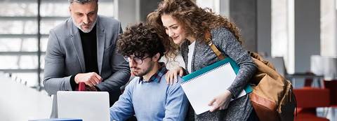 Un grupo de tres personas colabora frente a una computadora portátil en un espacio moderno.