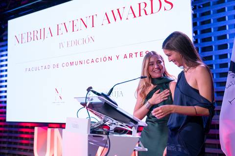Dos mujeres sonrientes se encuentran en un evento de premios en una ceremonia elegante.