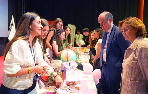 Un grupo de jóvenes presenta sus proyectos en un evento, mientras adultos observan atentos.