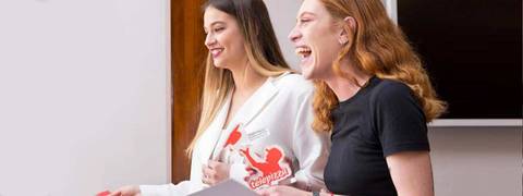 Dos mujeres sonrientes participan en una actividad, mostrando tarjetas y disfrutando del momento.