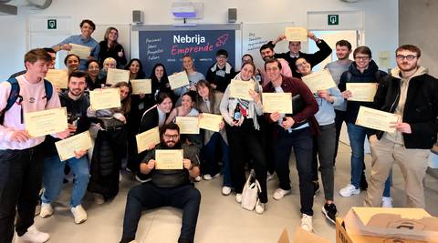 Un grupo de estudiantes sonrientes sostiene certificados frente a una pared decorativa en un evento de emprendimiento.
