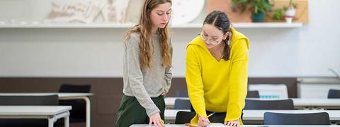 Dos mujeres colaboran en un trabajo en un aula moderna.