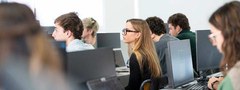 Un grupo de estudiantes en un aula frente a computadoras.